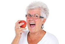 elderly woman biting into a red apple 